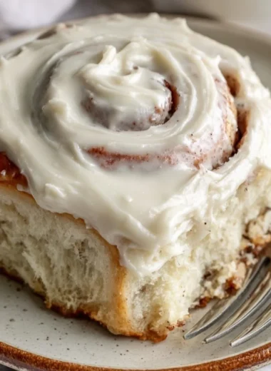 Freshly baked cinnamon rolls topped with icing on a wooden table
