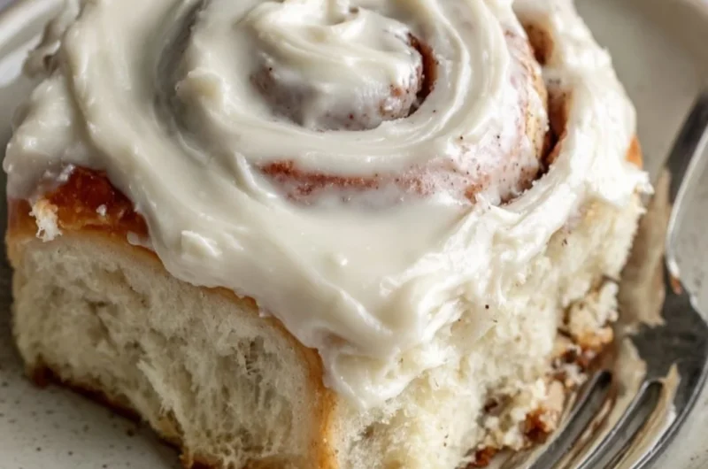 Freshly baked cinnamon rolls topped with icing on a wooden table