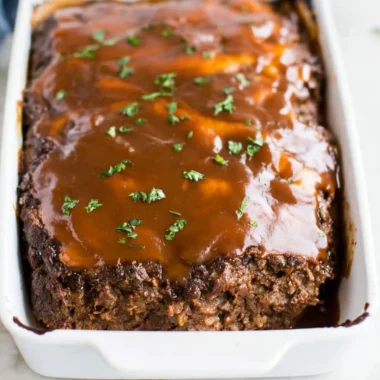 Classic meatloaf with brown gravy served on a plate, garnished with herbs.