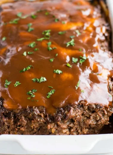 Classic meatloaf with brown gravy served on a plate, garnished with herbs.