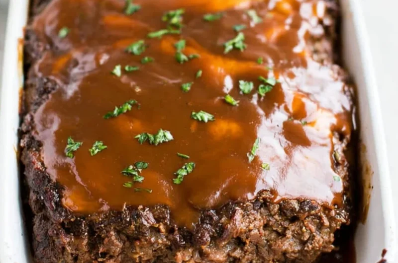 Classic meatloaf with brown gravy served on a plate, garnished with herbs.