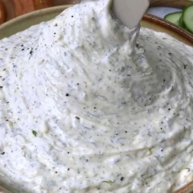 A creamy cucumber dip served in a bowl garnished with herbs.