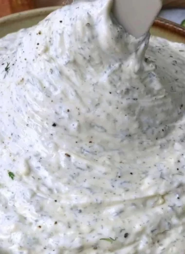A creamy cucumber dip served in a bowl garnished with herbs.