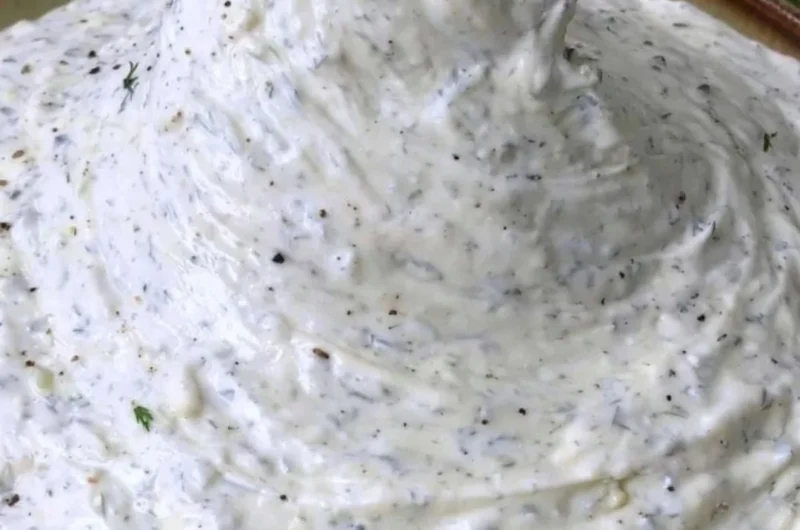 A creamy cucumber dip served in a bowl garnished with herbs.