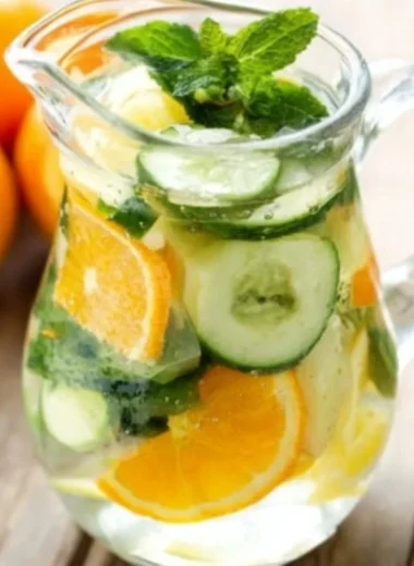 Glass of orange cucumber mint water on a wooden table