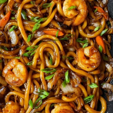 A plate of stir-fried udon noodles with vibrant vegetables and proteins.
