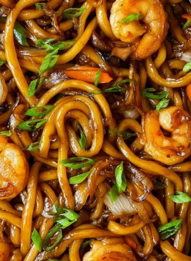A plate of stir-fried udon noodles with vibrant vegetables and proteins.