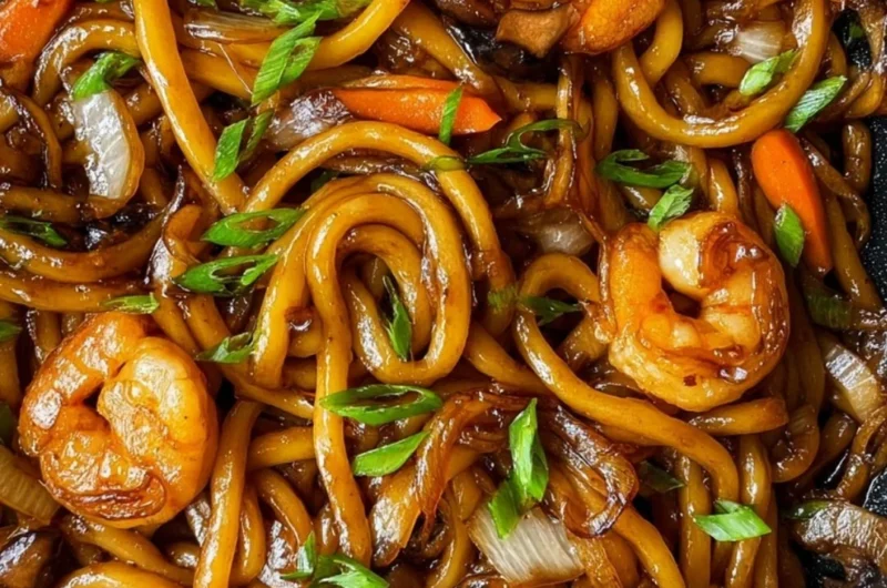 A plate of stir-fried udon noodles with vibrant vegetables and proteins.